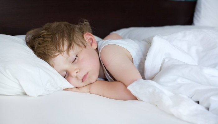 A cute little boy asleep in his bed with white bedding.