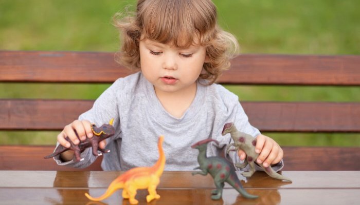 A little girl sitting at a table outside playing with toy dinosaurs.