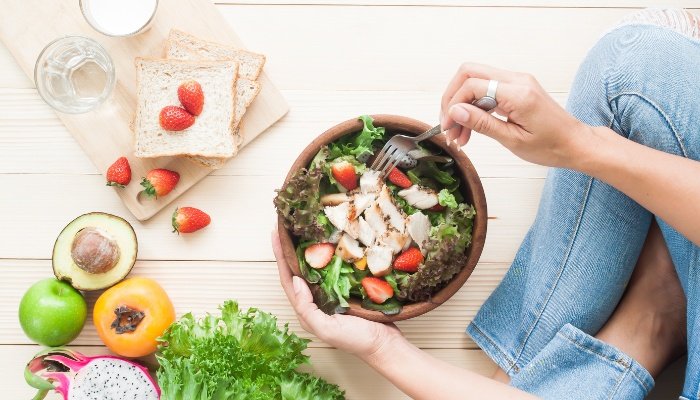 Woman sitting on floor eating a healthy salad.
