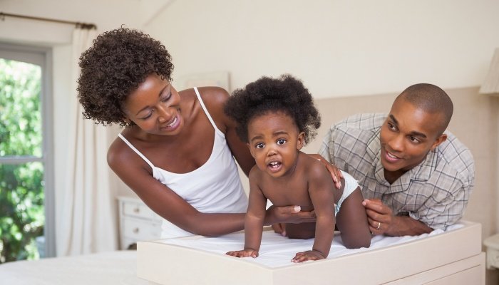 A mother and father working together to change their toddler's diaper.