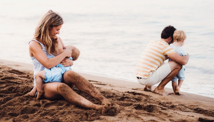 A mother at the beach with her family pauses to nurse her baby.