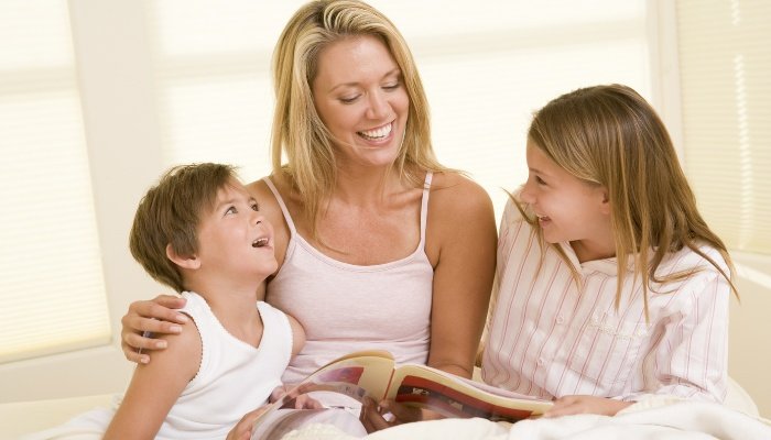 A young mother reading to her children while they snuggle together in bed.