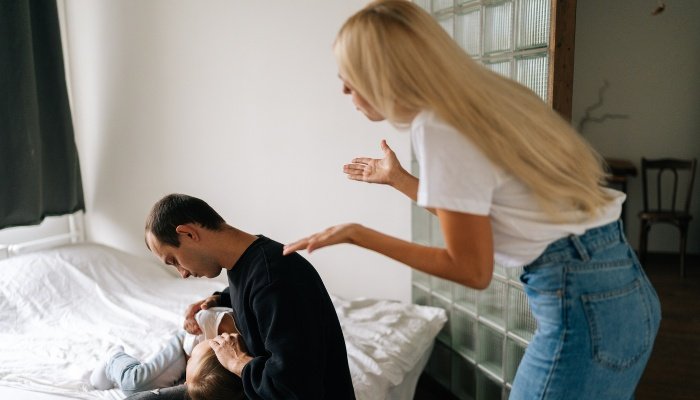 A mother yelling at a father who is sitting on the bed comforting their daughter.