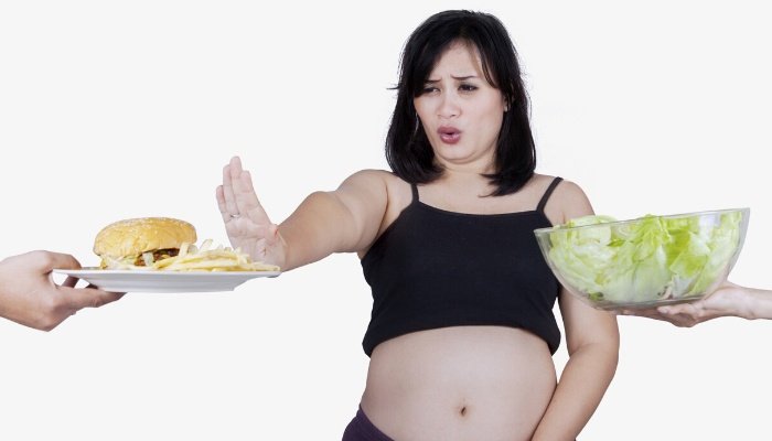 A pregnant woman refusing a plate with a burger and fries while holding her stomach.