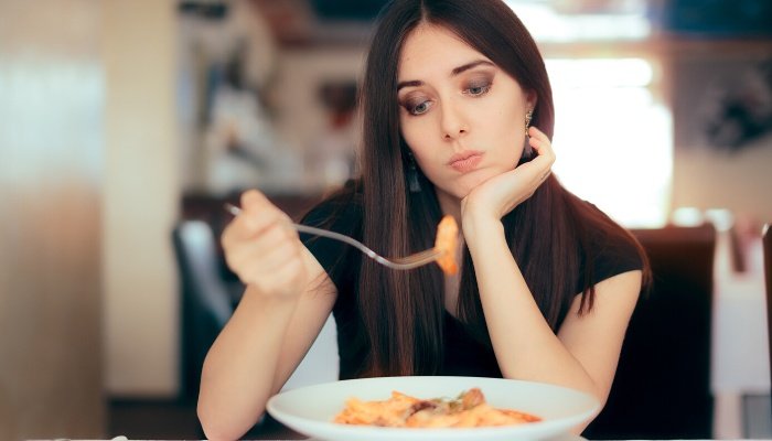 A pregnant lady looking uninterested at the food on her fork.
