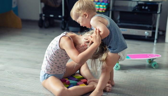 An agry toddler attempting to hurt his big sister by pulling hair.