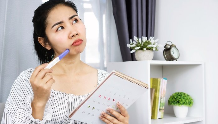 A young woman holding a pregnancy test and a calendar wondering if the time is right.