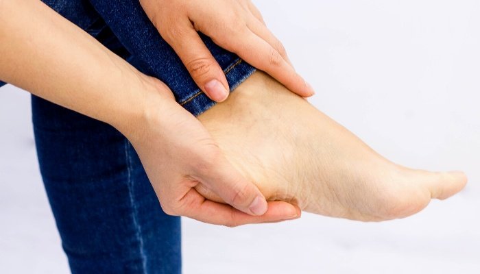 A pregnant woman holding her aching, sore foot.
