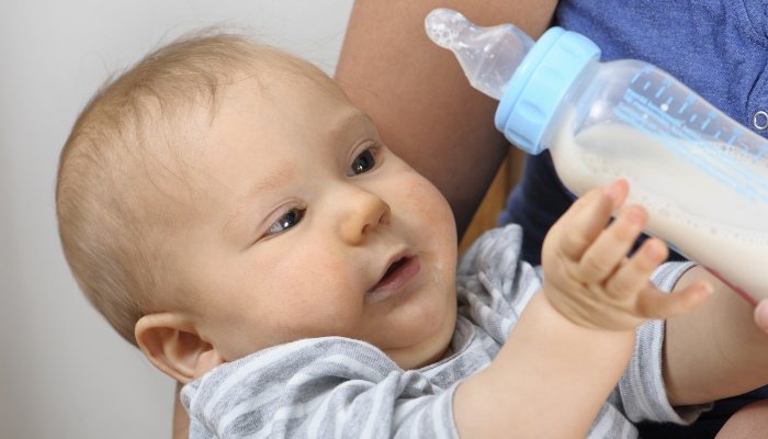 A baby pushing the bottle away from himself.