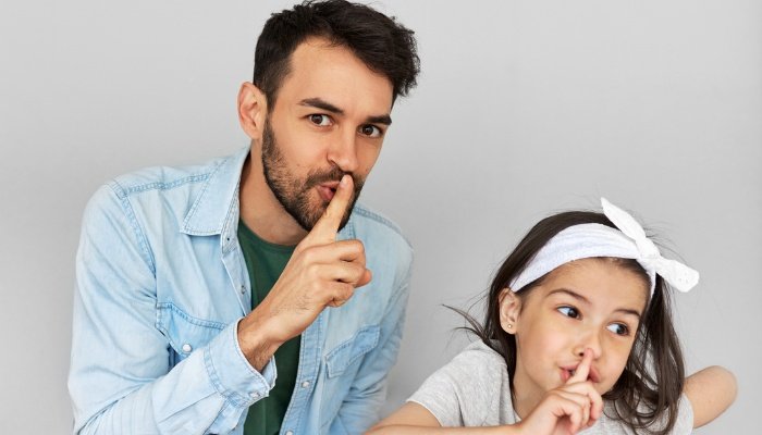 A dad and his daughter making the quiet gesture because they have a secret.