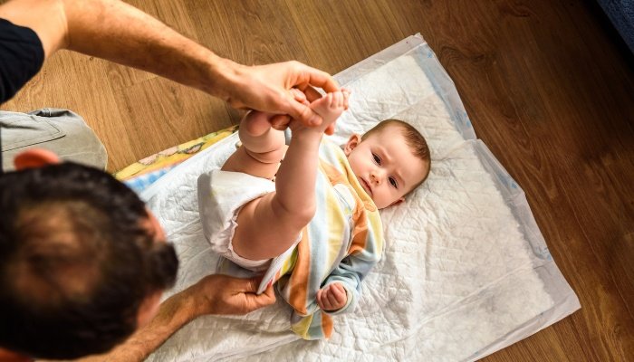 A father changing his baby's dirty diaper on the floor.