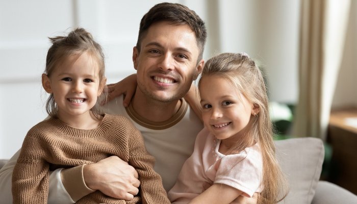 A dad hugging his two daughters at home on a couch.