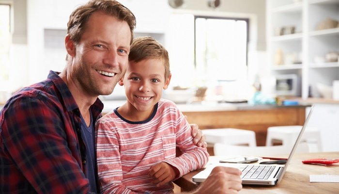 A father smiling with his son on his lap after working on his laptop.