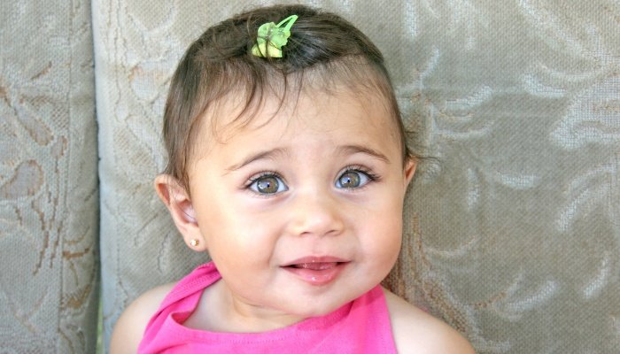 A little girl with big brown eyes and pierced ears.