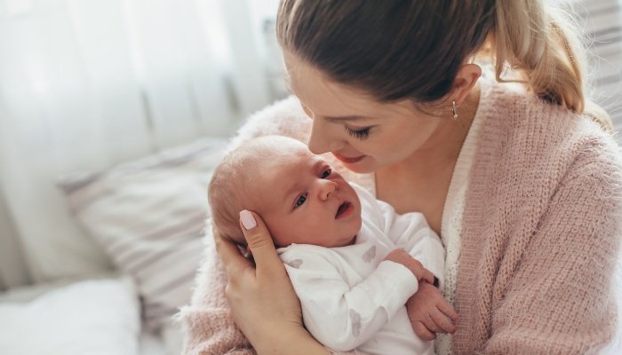 A young mother with her hair in a ponytail holding her newborn baby.