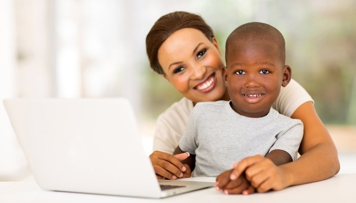A mother and her young son smiling as they work on a laptop.