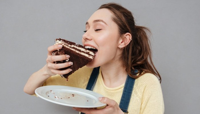 A hungry pregnant woman eating chocolate cake with her hands.