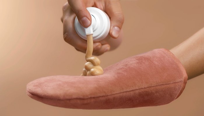 Self-tanning lotion being squirted on an application mitt.