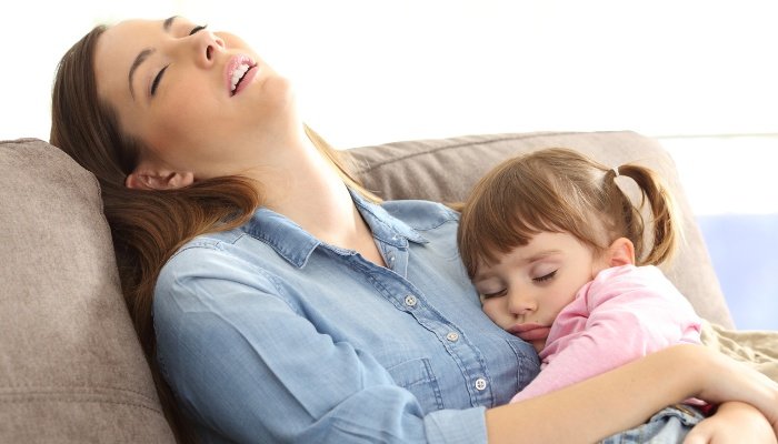 A tired mom dozes while holding her sleeping toddler.
