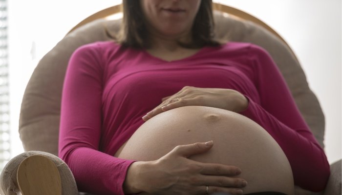 A very pregnant woman sitting in a chair cradling her large belly.