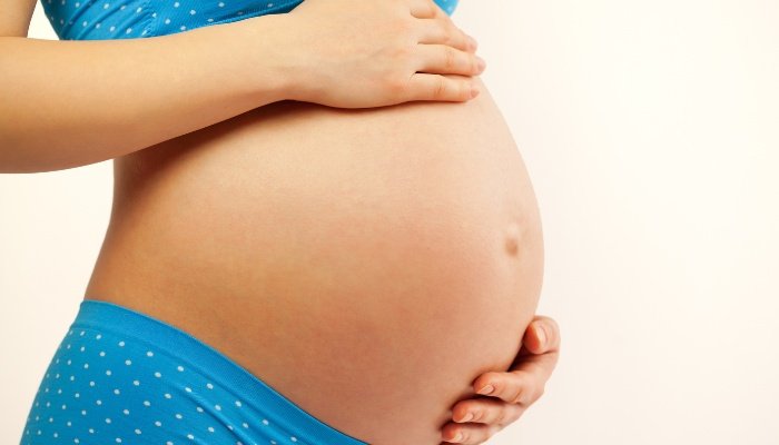 A woman wearing light blue underwear with white polka dots holding her pregnant belly.