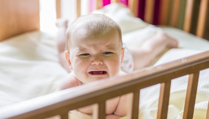 A baby girl lying on her tummy in her crib and crying.