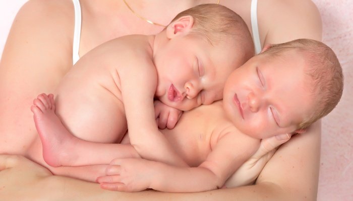 A mother holding her naked twin babies in her arms.