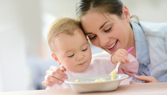 A young mother giving her baby a hug while baby feeds herself lunch.