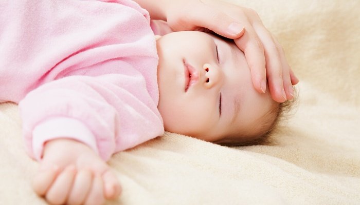 A mother's hand resting on her sleeping baby's forehead to check for overheating.