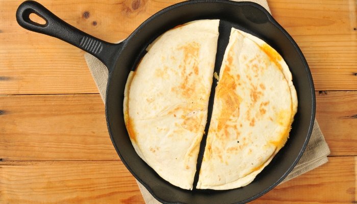 A cheese quesadilla cut in half in a cast iron skillet.