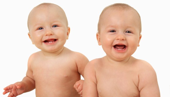 Twin baby girls sitting up and smiling.