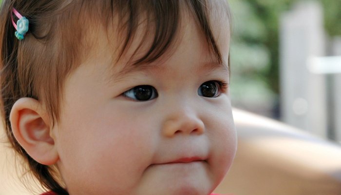A cute baby girl wearing a barrrette and sucking her bottom lip.