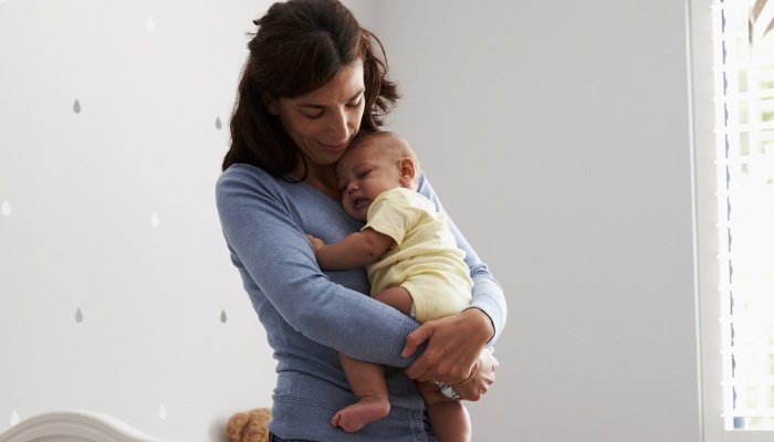 A mother standing in the nursery holding and comforting her infant.