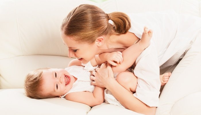 A young mother tickling her happy baby on the couch.