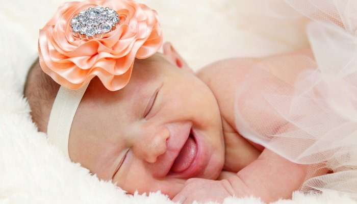 A newborn baby girl wearing a headband laughing in her sleep.
