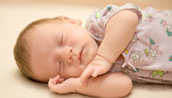 A baby girl sleeping on her side in pink bunny-print pajamas.