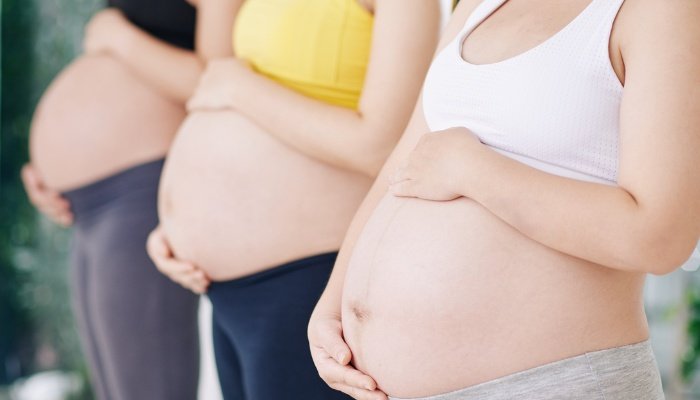 Three pregnant women in yoga clothes standing in a row.