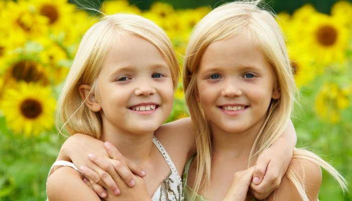 Blonde twin sisters hugging in front of sunflowers.