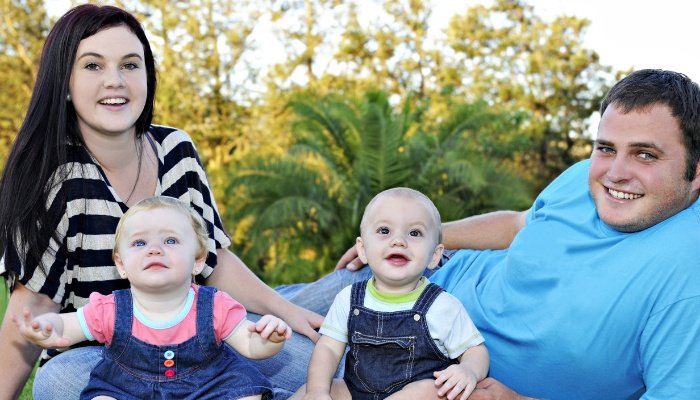 A husband and wife sitting with their fraternal twin babies outside.