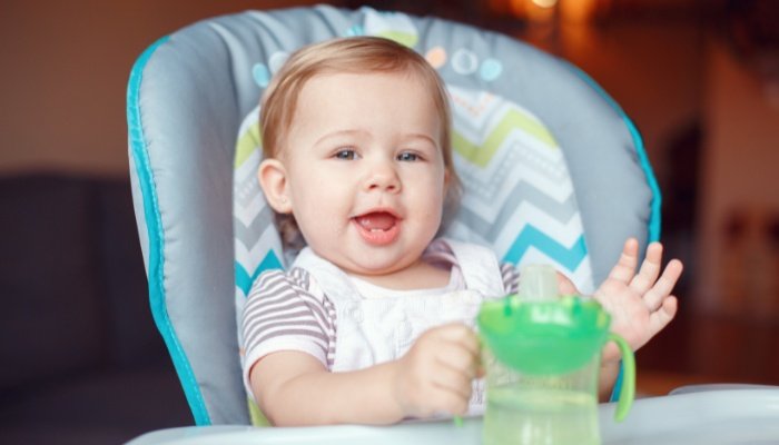 A cute little girl with a sippy cup sitting in her high chair.