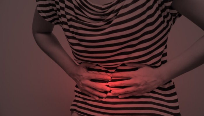 Black-and-white shot of woman holding her belly in pain with red lighting over her hands.
