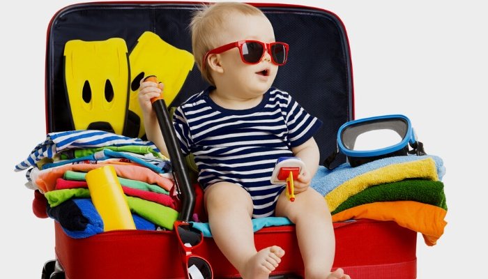 A cute toddler wearing sunglasses sitting inside an open suitcase ready for a trip.