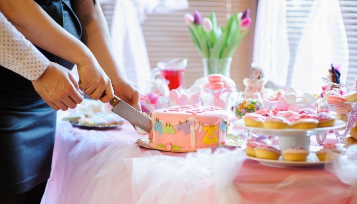 The dessert table at a baby shower with parents cutting the cake.