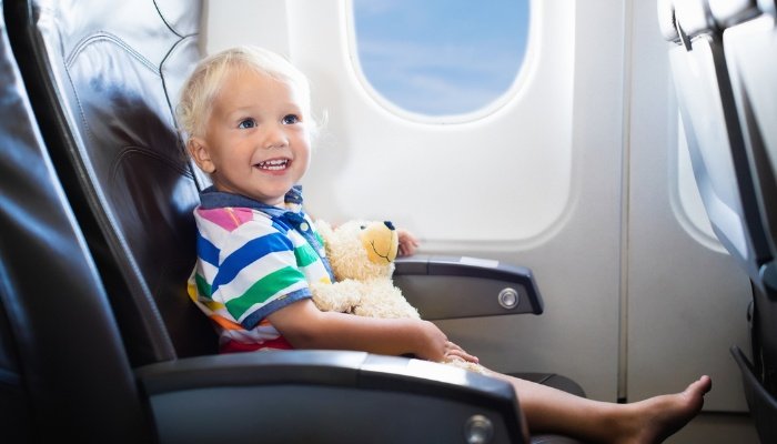 A happy toddler on an airplane with bare feet and a teddy bear.