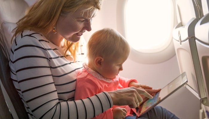 A mother and her toddler on an airplane passing the time with a tablet.