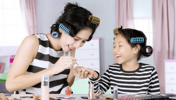 A mother painting her daughter's nails while they wear curlers in their hair.