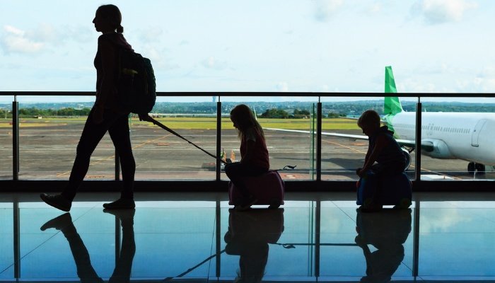 A mother at an airport pulling her two children behind her while they ride on kid seats.