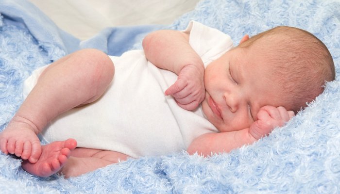 A newborn baby boy in a white onesie lying on a blue blanket.