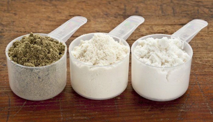 Three scoops of different protein powders on a wood table.