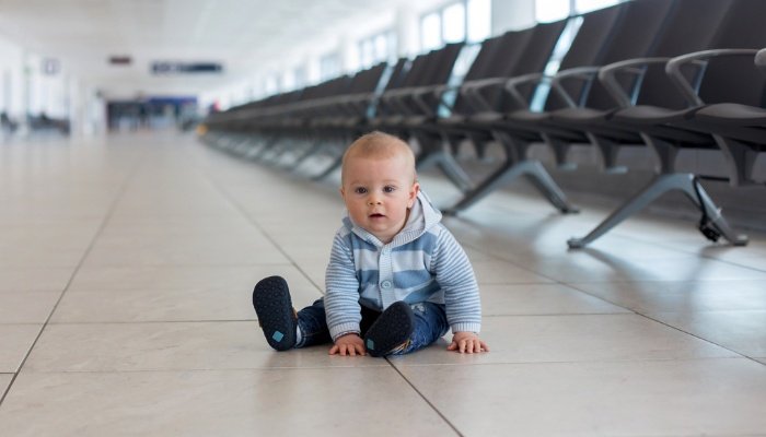 A toddler sitting on the floor at the airport while waiting to board the plane.